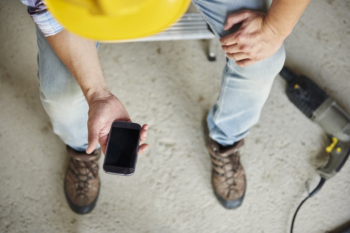 Tradesperson looking for missed calls ai voice agents for trade services in jeans and steel-cap boots holding a phone, with a hard hat and drill on the ground nearby